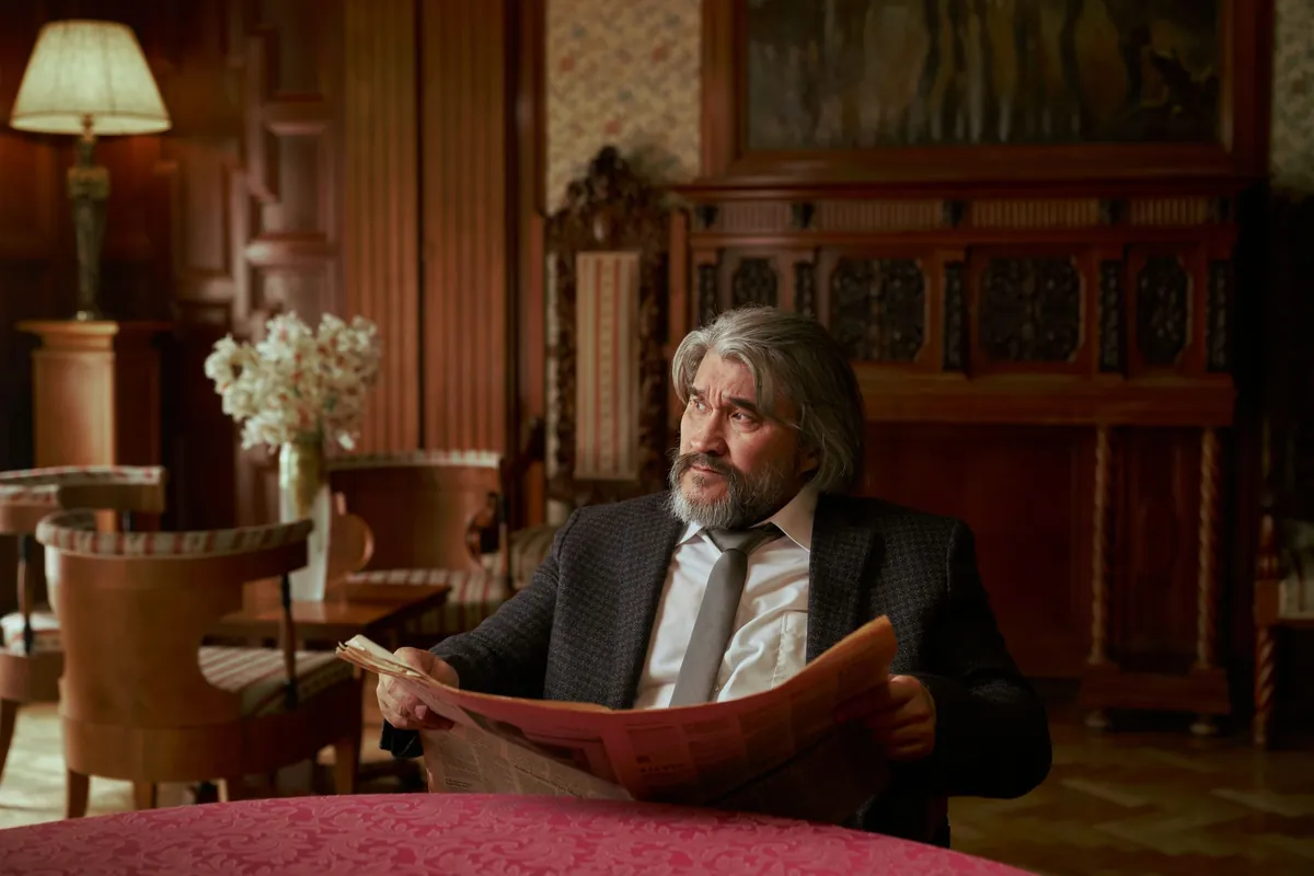 Silver-haired man reading a newspaper in a wood-paneled lounge