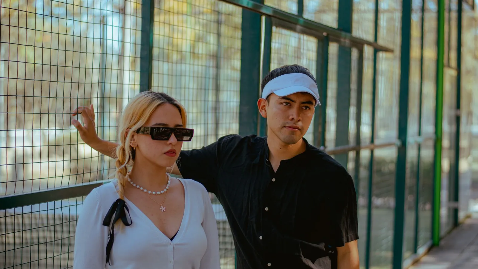 Stylish couple in sunglasses and tennis whites posing on a sunny tennis court
