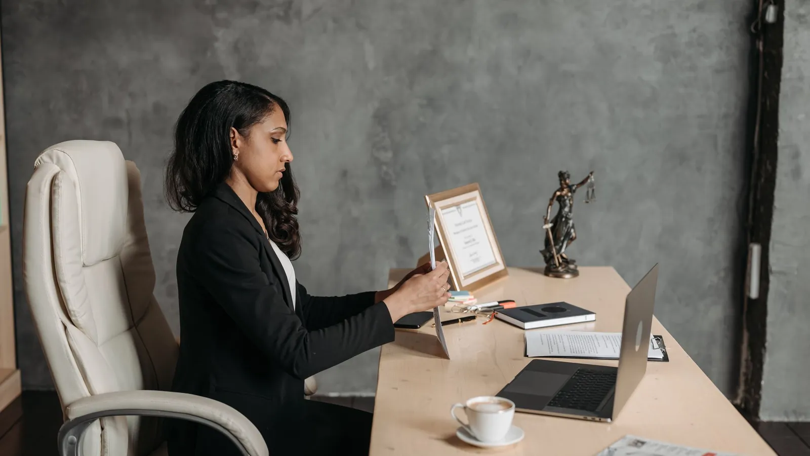 Businesswoman in formal attire working at a laptop in a contemporary office with a leather chair