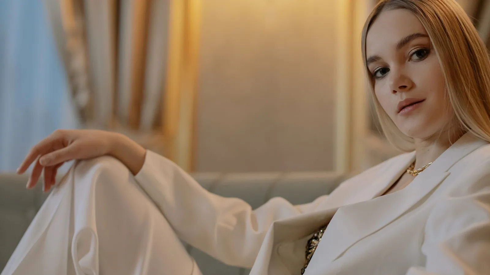 Woman in a white silk suit reclining on a sofa in soft golden light