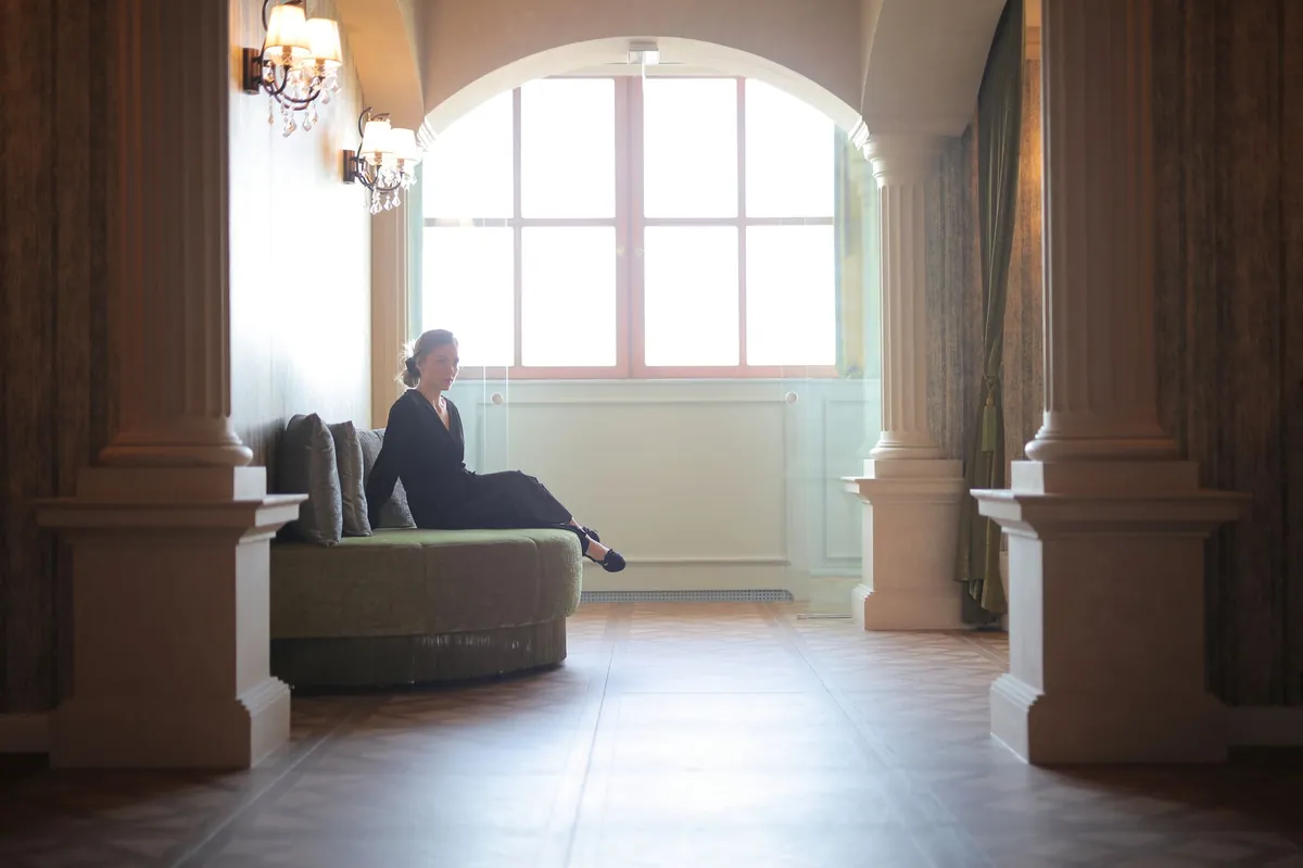Woman in a black dress seated in a classic lobby framed by columns and a tall arched window