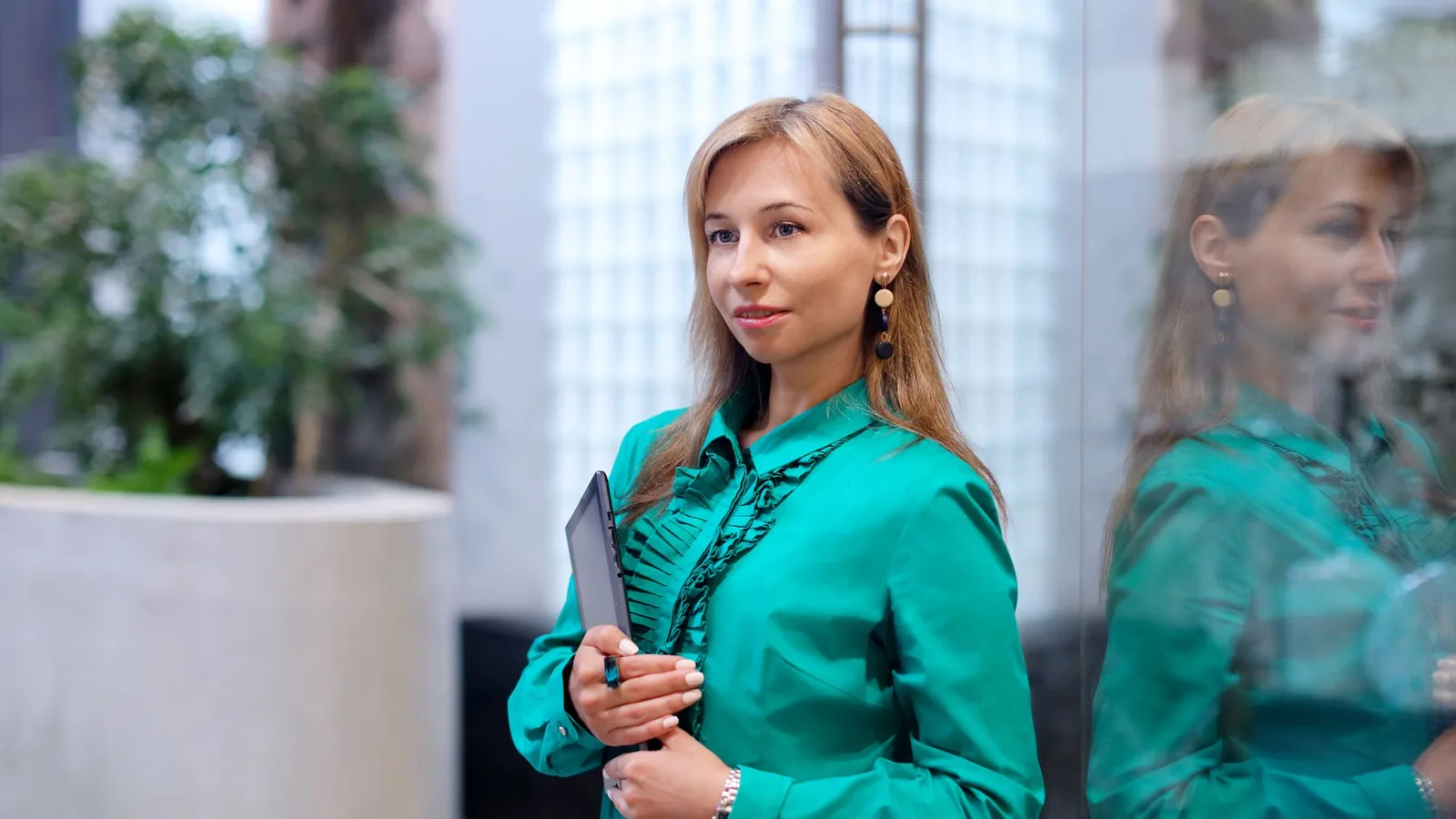 Confident woman in an emerald silk blouse in a bright modern lobby