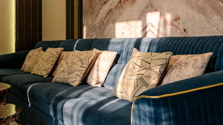 Deep blue velvet sofa with patterned cushions against a warm marble wall