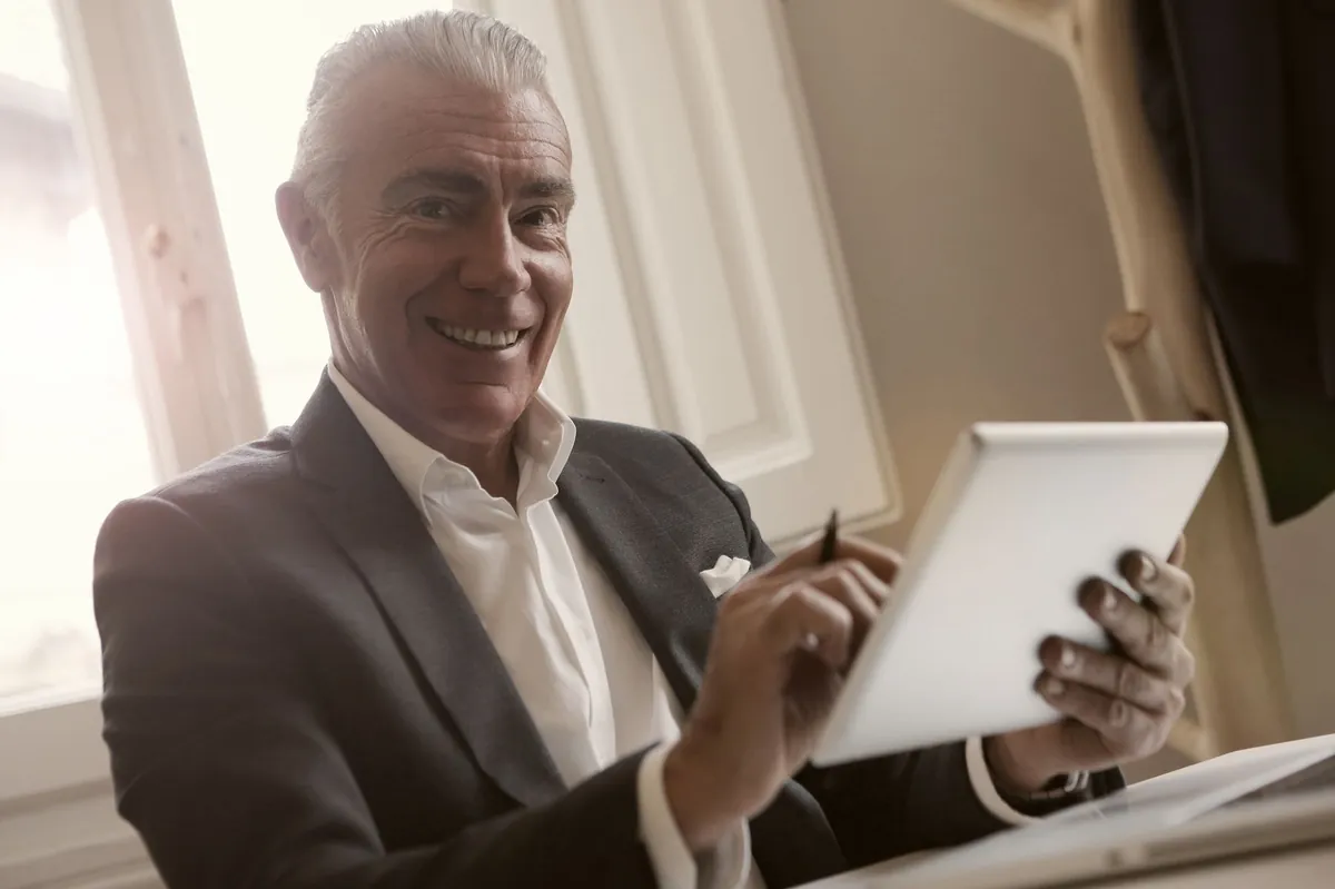 Smiling silver-haired businessman in a suit reviewing a tablet in a bright office