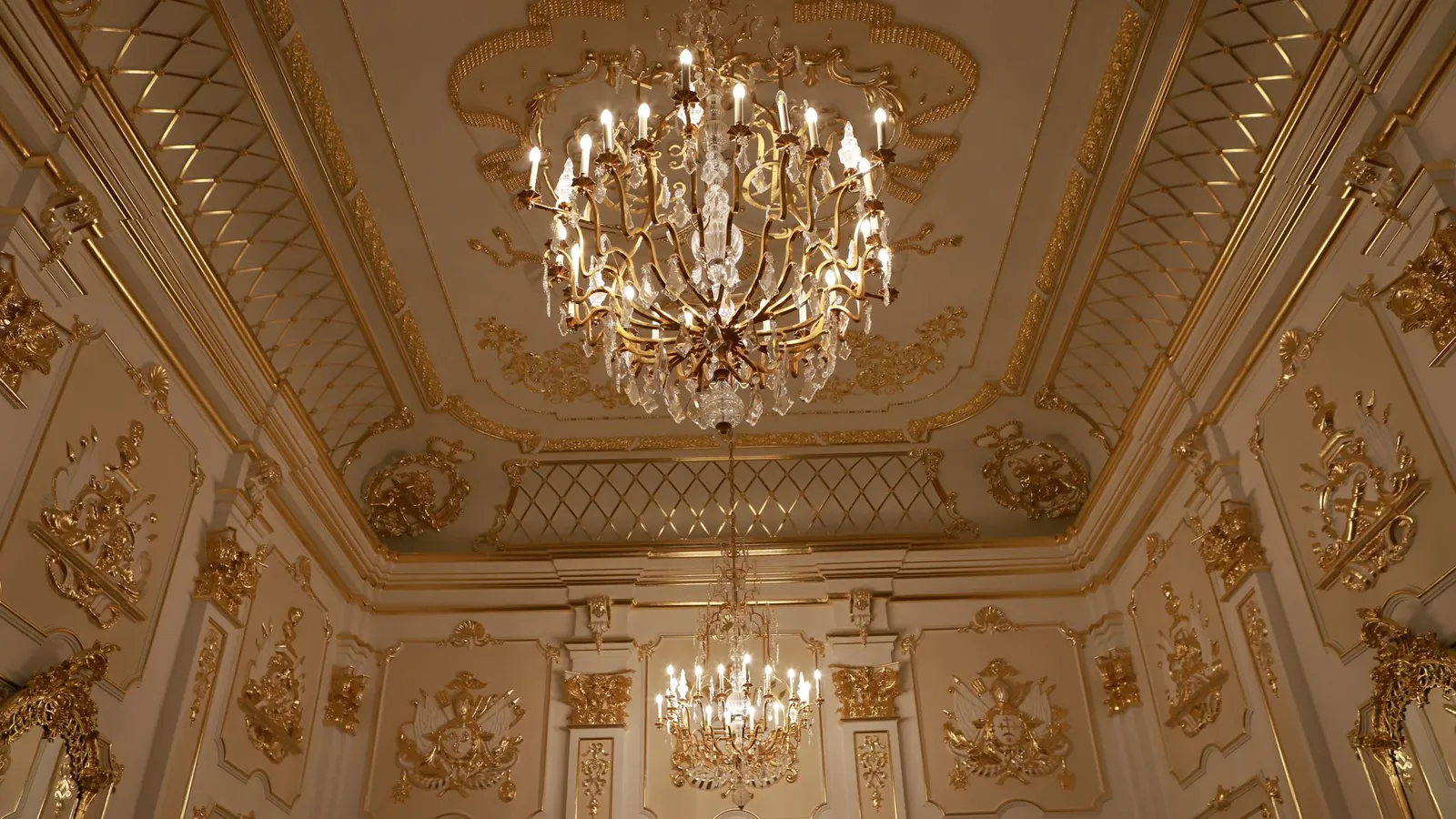 Ornate gold ballroom ceiling with two crystal chandeliers