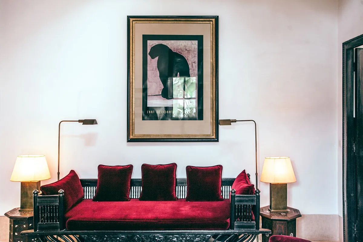 Crimson velvet daybed framed by brass reading lamps and framed art
