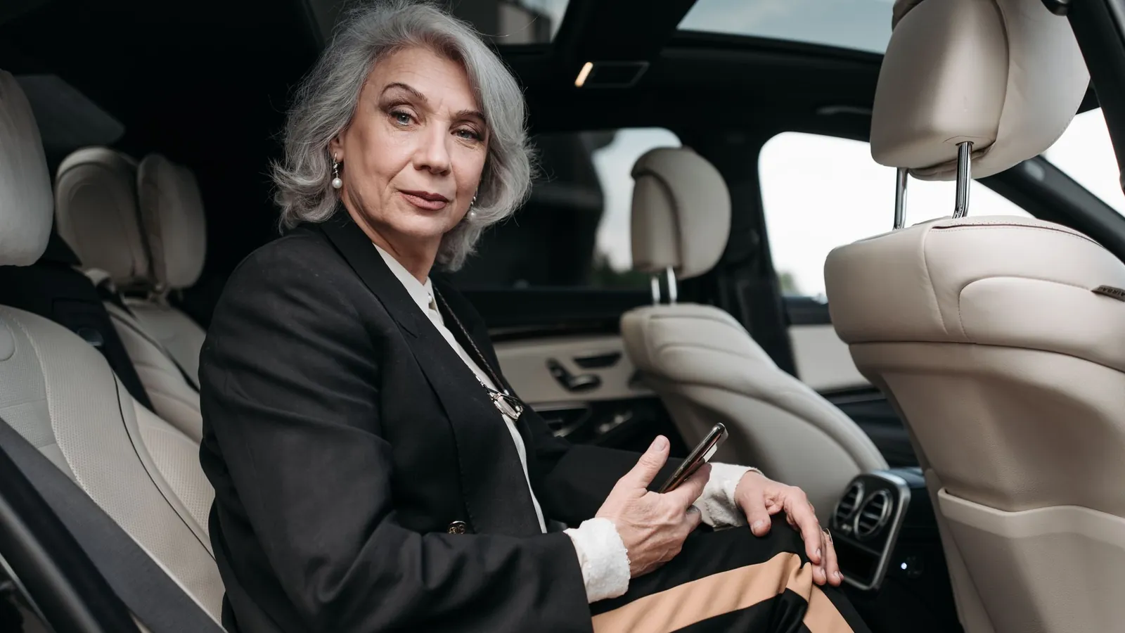 Silver-haired businesswoman in a tailored suit using her phone in the back of a luxury car