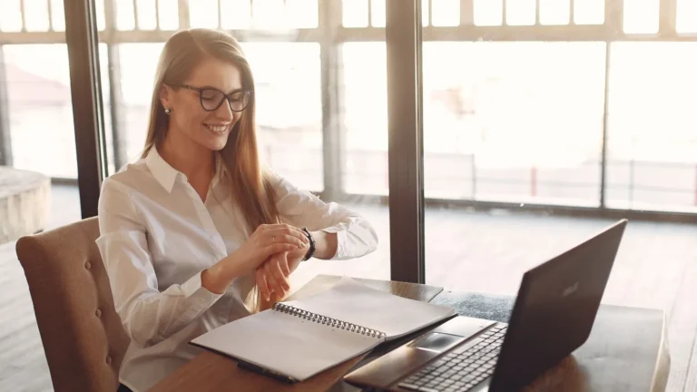 Smiling entrepreneur in eyeglasses working on a laptop by tall windows