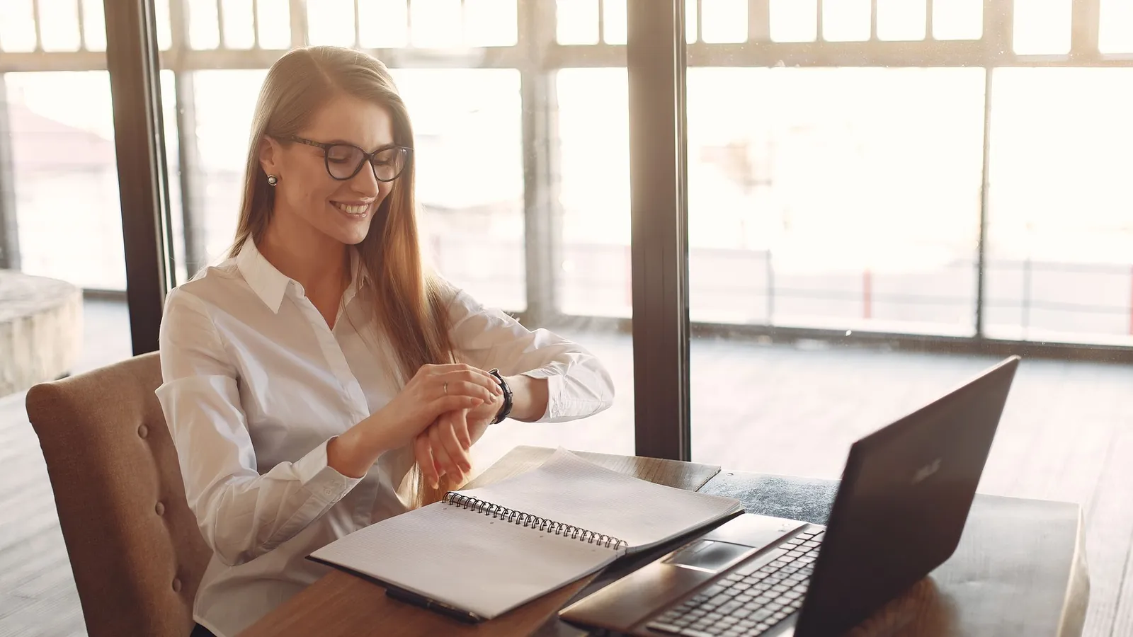 Smiling entrepreneur in eyeglasses working on a laptop by tall windows