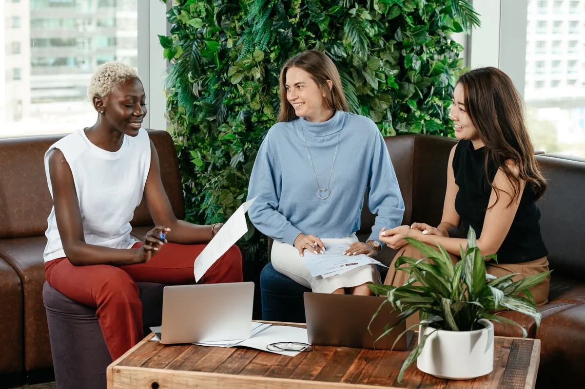 Three colleagues talking over papers at a table in front of a green plant wall