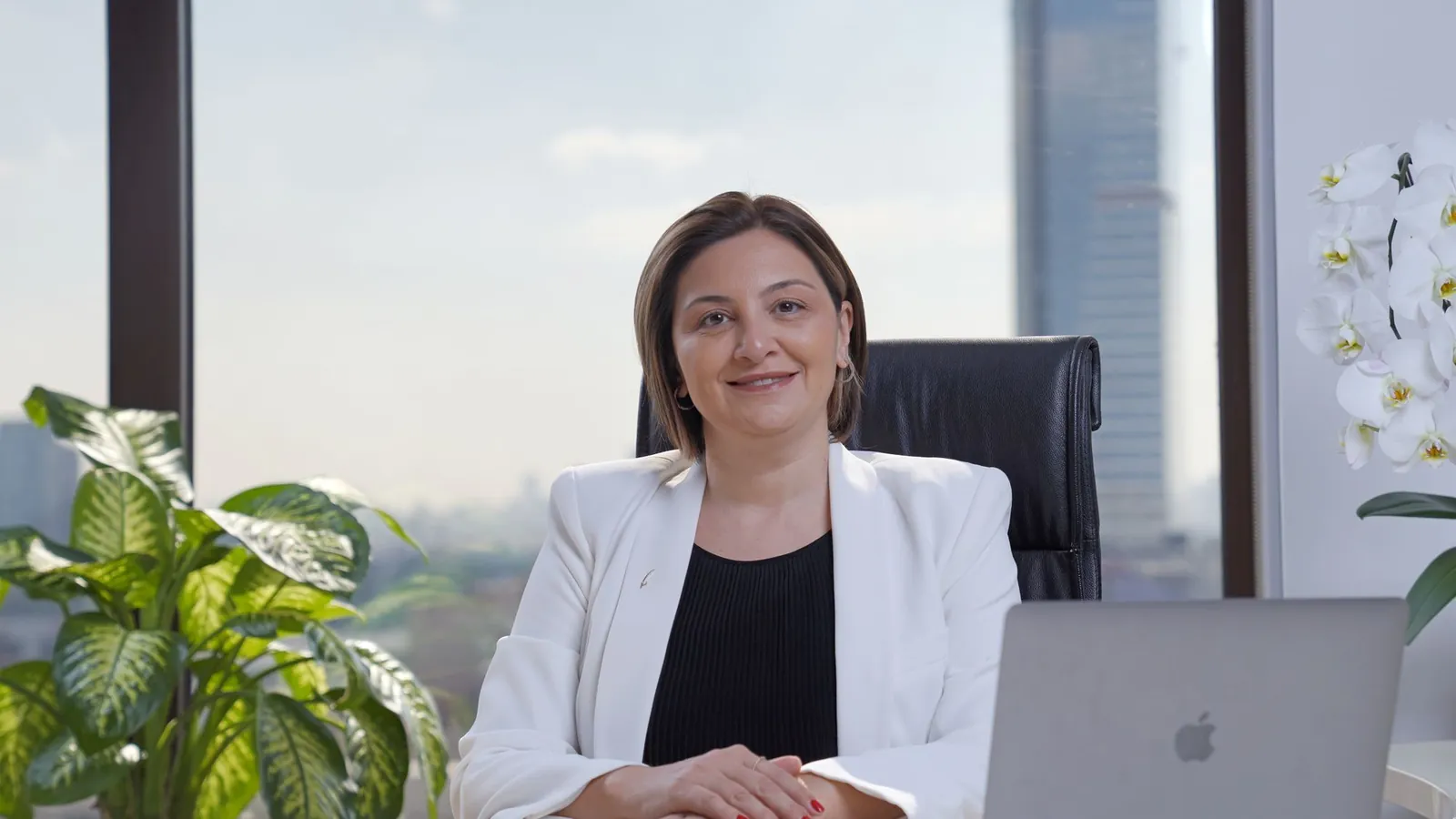 Confident professional in a white suit at a desk with a laptop in a refined modern office