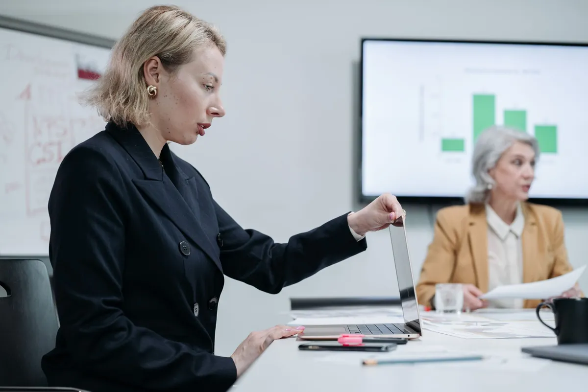 Two professionals reviewing charts and data together on a laptop in a bright office