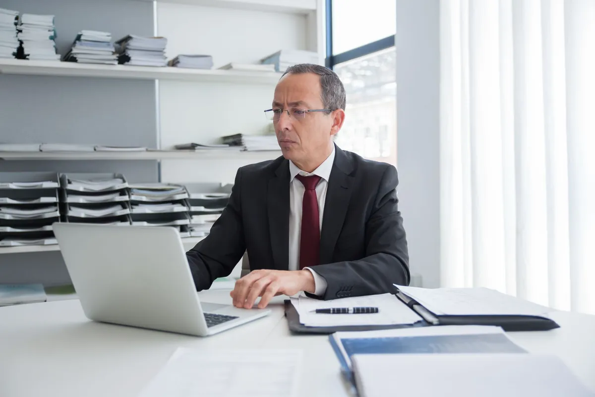 Professional in a suit working at an office desk with a laptop and documents