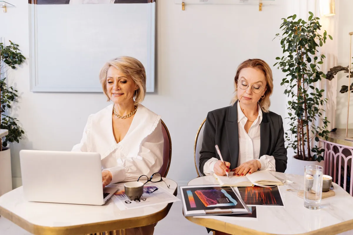 Two professional women reviewing paperwork together at a white desk in a bright office