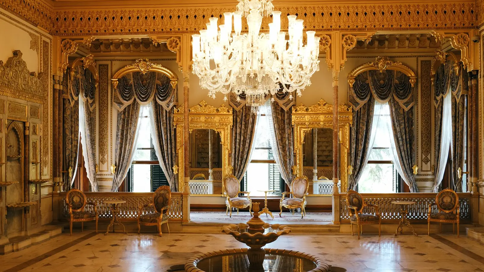 Gilded hall with crystal chandelier, tall draped windows and a marble fountain