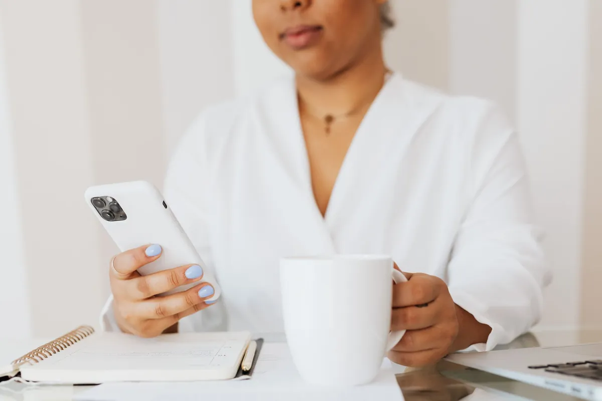 Woman in a white shirt using her phone while holding a coffee cup