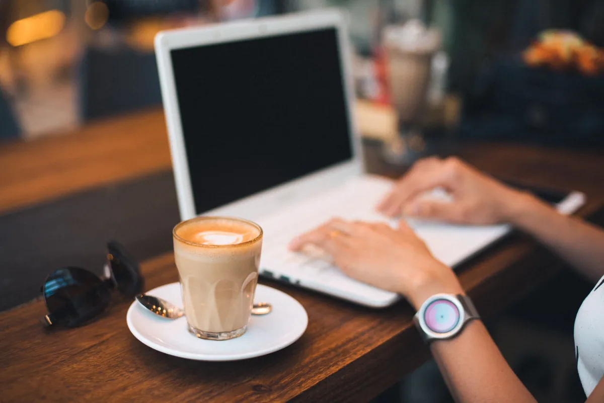 Hands typing on a laptop beside a latte, planning clinic patient communications