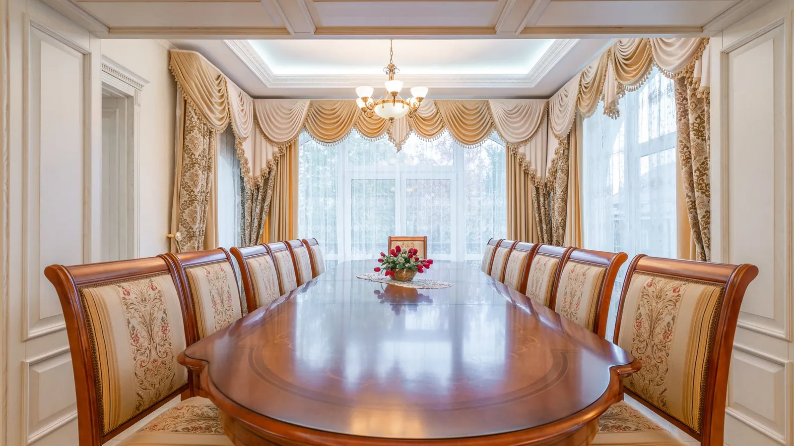 Formal dining room with a polished oval table and gold drapes