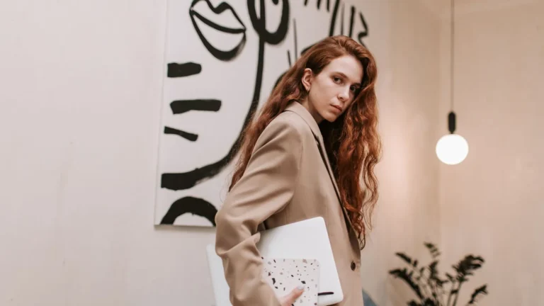 Clinic owner in a camel blazer carrying a notebook through a modern gallery-style office